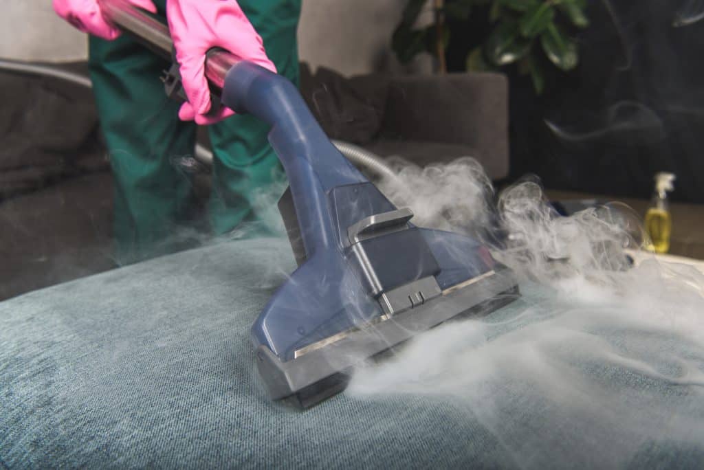 person cleaning sofa with vacuum cleaner